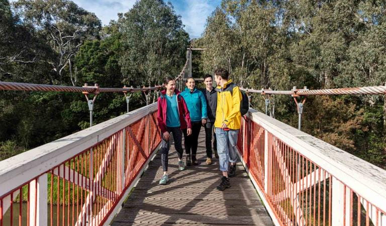Four friends walk across Kanes Bridge over the Yarra River near Studley Park Boathouse