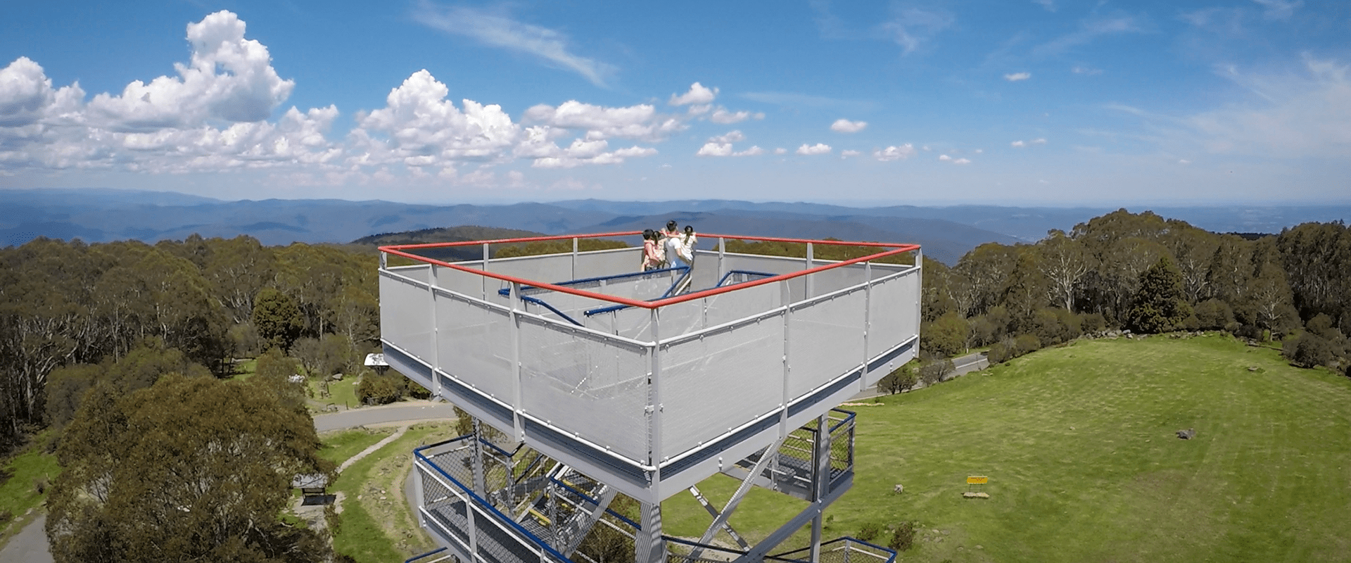 A family looks out from the Mount Donna Buang tower looking out towards endless forested mountain range.