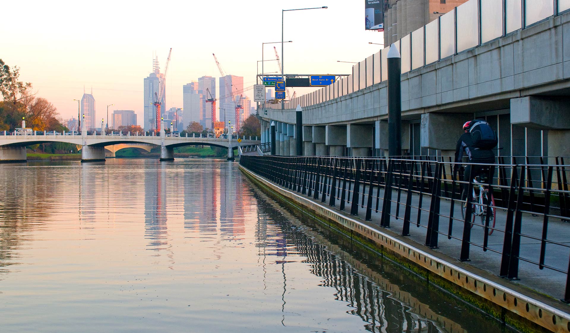 A cyclist follows the bike path along the Yarra River heading in to the Melbourne CBD at sun set.