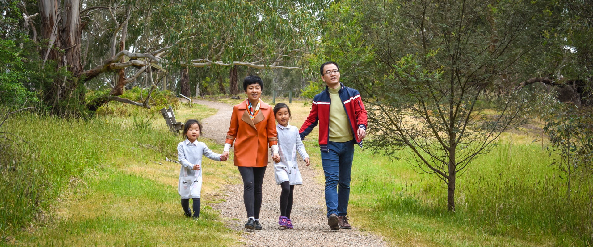 A family walk down a paved path surrounded by green grass and mature trees.