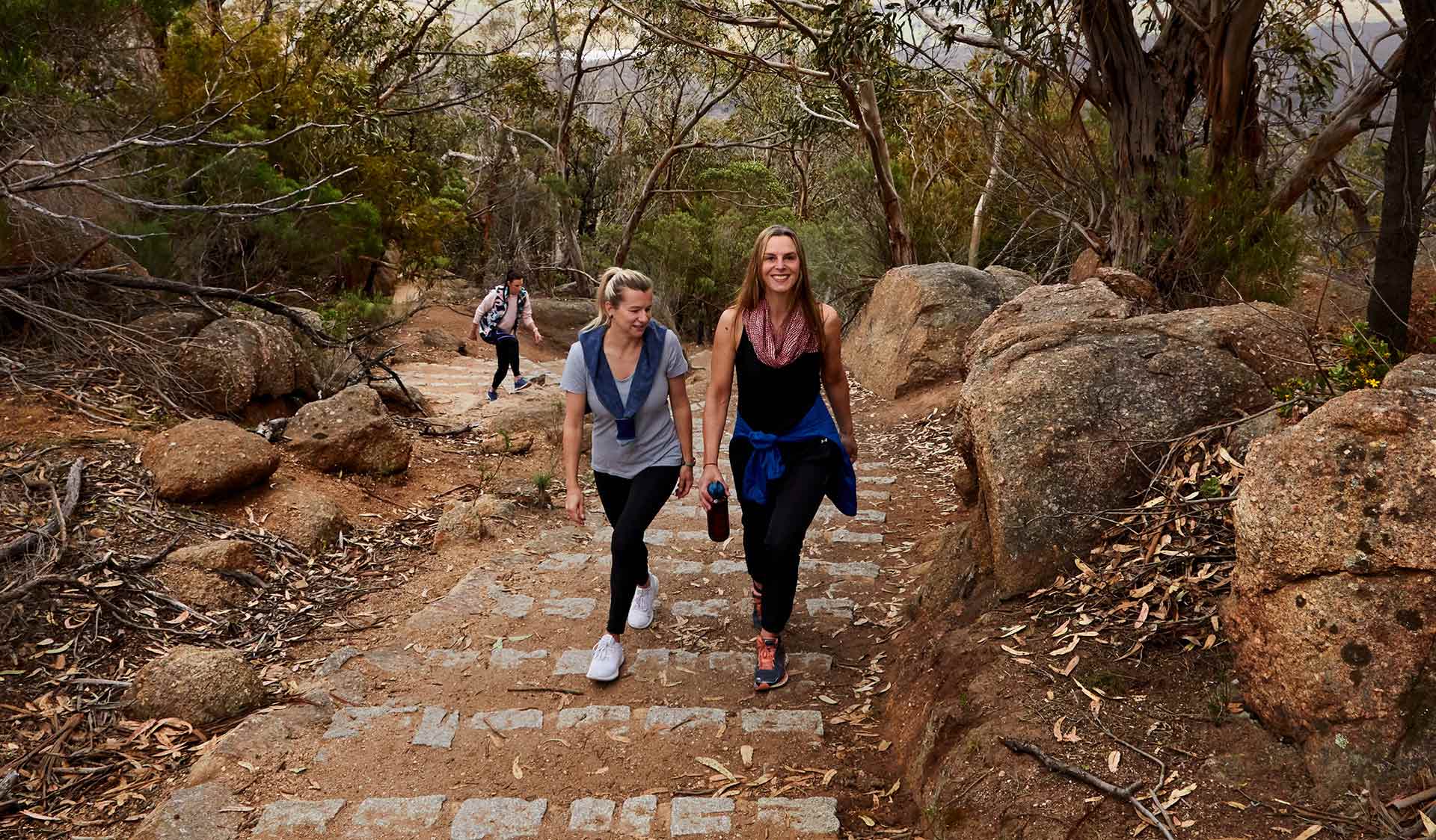 Two women in active wear walk up the granite steps on the way to Flinders Peak.