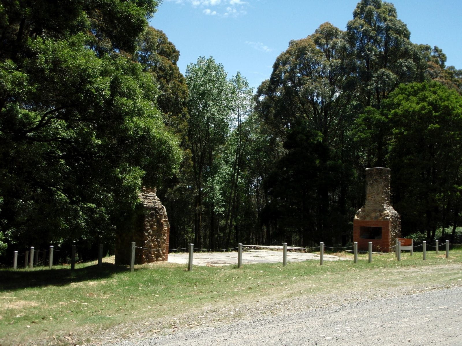 A historical site featuring 2 brick entry gates. There are large trees behind them. 