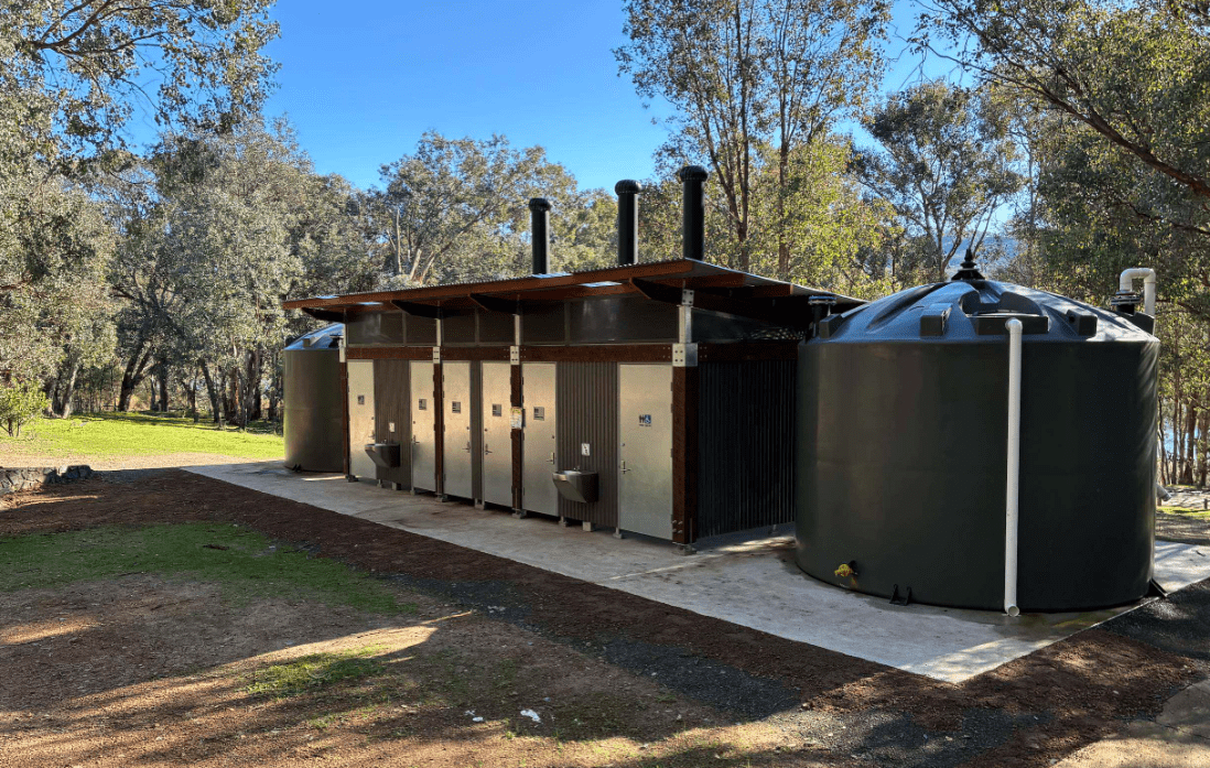 Updated Lakeside Campground toilet block featuring multiple cubicles, accessible design elements, external handwashing facilities, rainwater harvesting tanks, and modern durable construction within a bushland recreation setting.