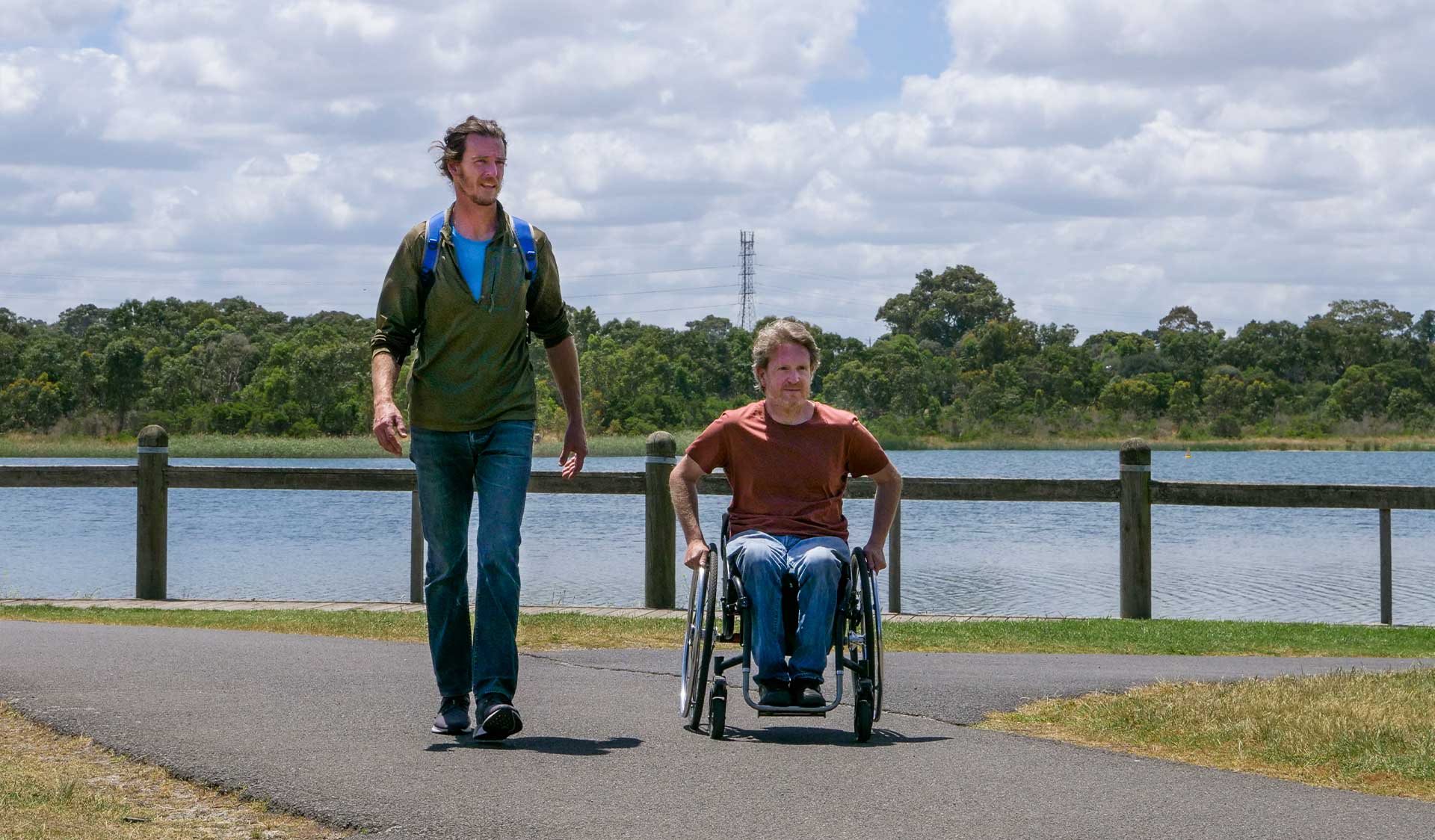 Two men, one in a wheelchair, walk away from the water's edge at Karkarook Park 