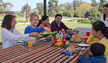 A group of adults and a child enjoy a barbecue at Toororrong Reservoir Park