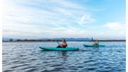 Two teenage girls kayaking on Mallacoota Inlet with mountains in the background.  
