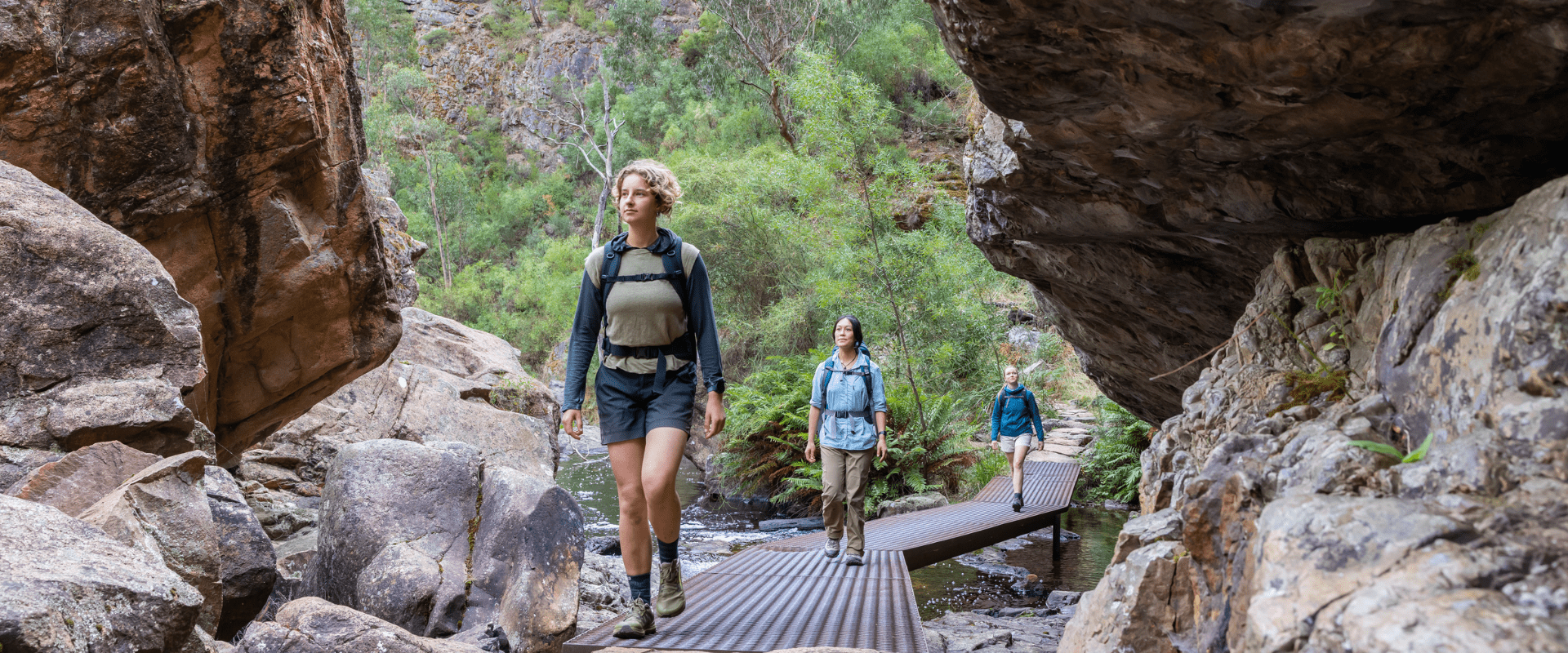Three hikers walking along boardwalk amongst big rocks.