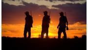 Three hunters silhouetted at sunset.