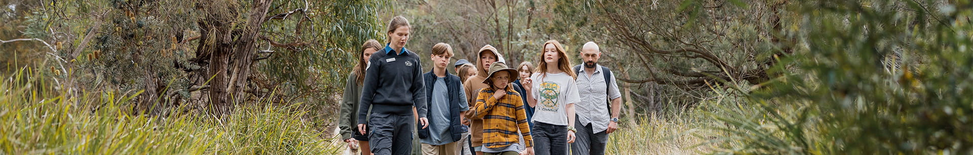 A ranger in uniform guiding a group of children and an adult along a path surrounded by bush at Ocean Grove. 