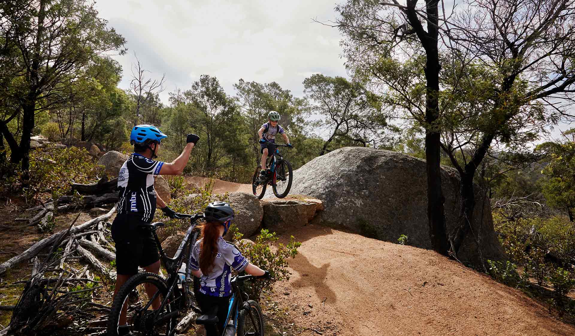 A young mountain biker attempts a drop while cheered on by his father and older sister at the You Yangs Regional Park.