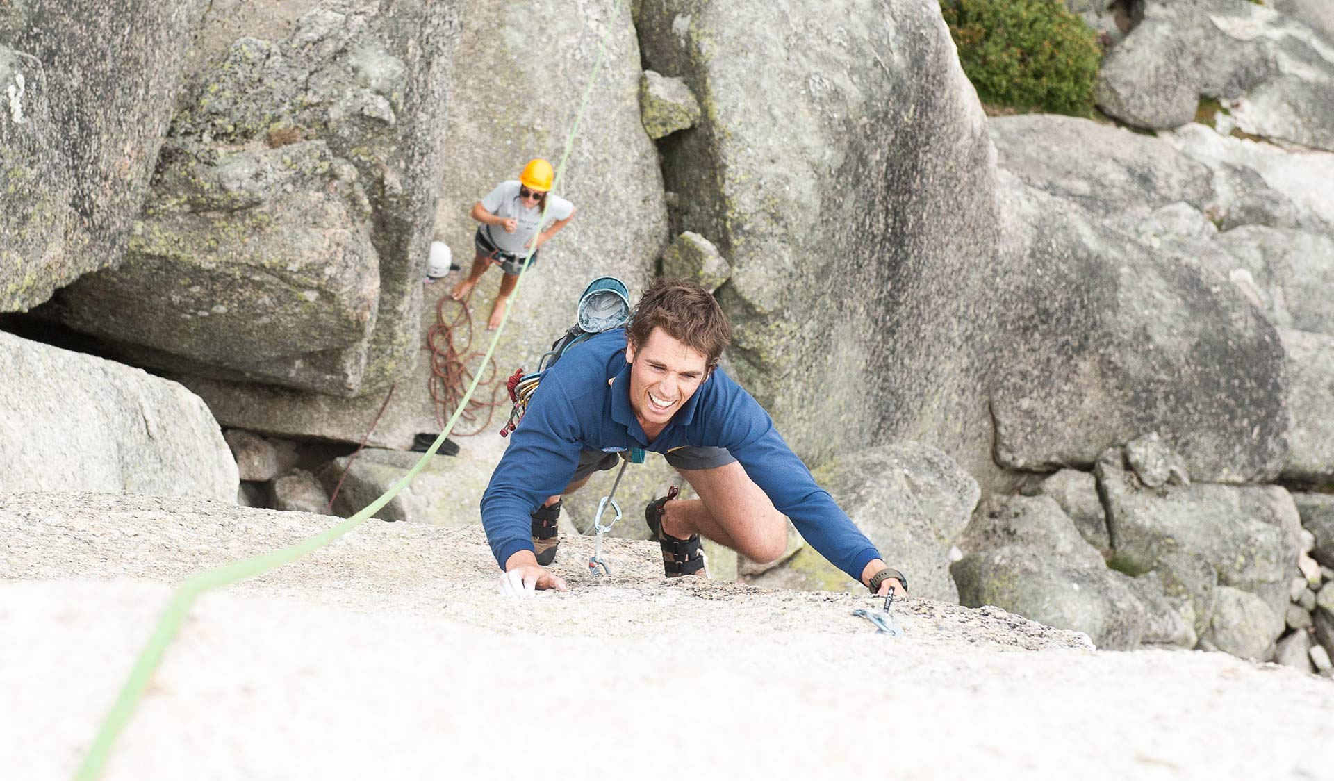 A young man climbs a near featureless wall at Mt Buffalo while his climbing partner watches on.