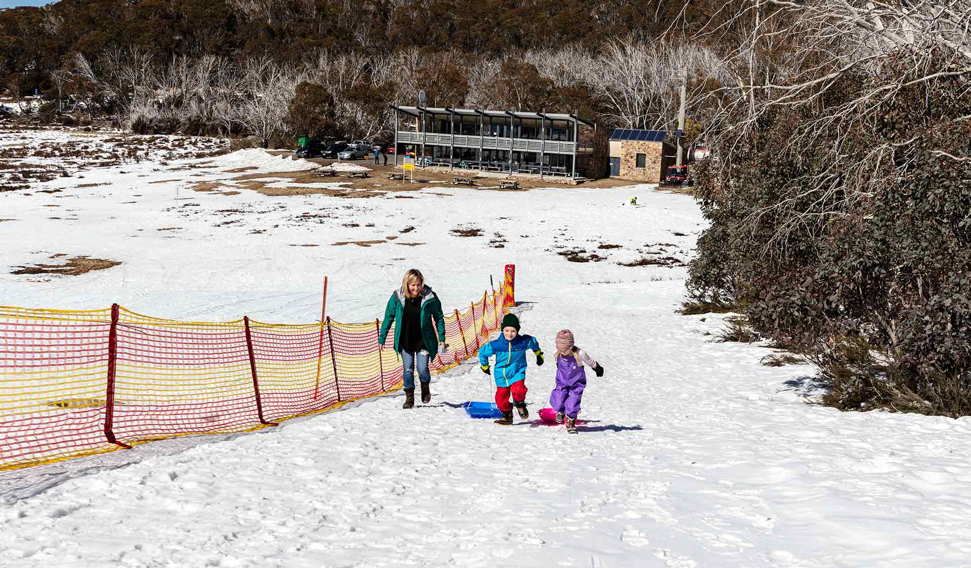 A mother and her two children climb to the top of the toboggan slope at Dingo Dell Mount Buffalo
