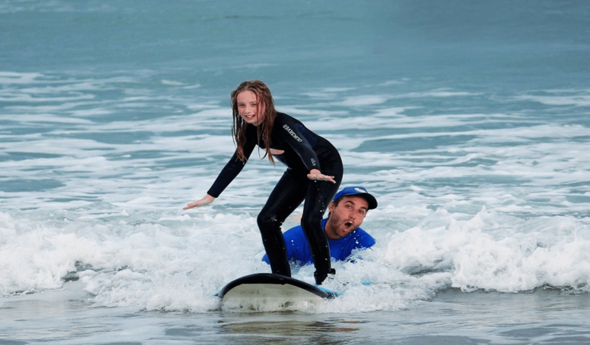 Surfing instructor assisting child on surfboard in the ocean.