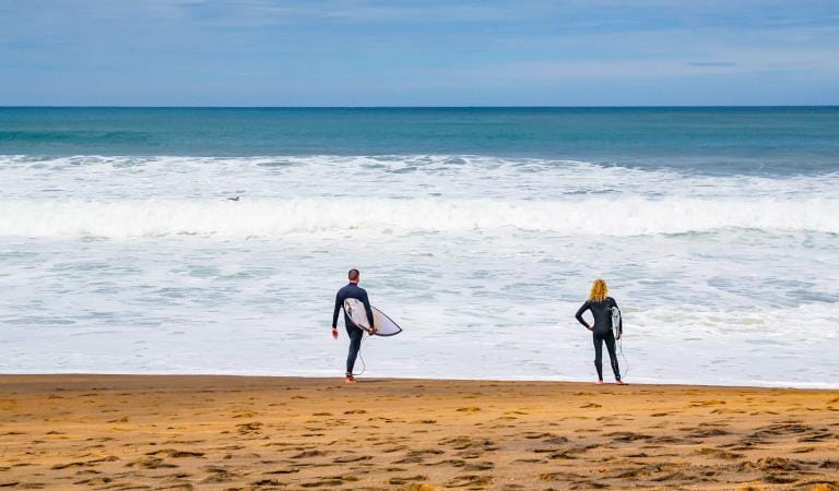 Two men with surfboards look out over the ocean