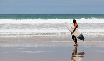 A man in a wetsuit holds his surfboard as he looks out over the ocean