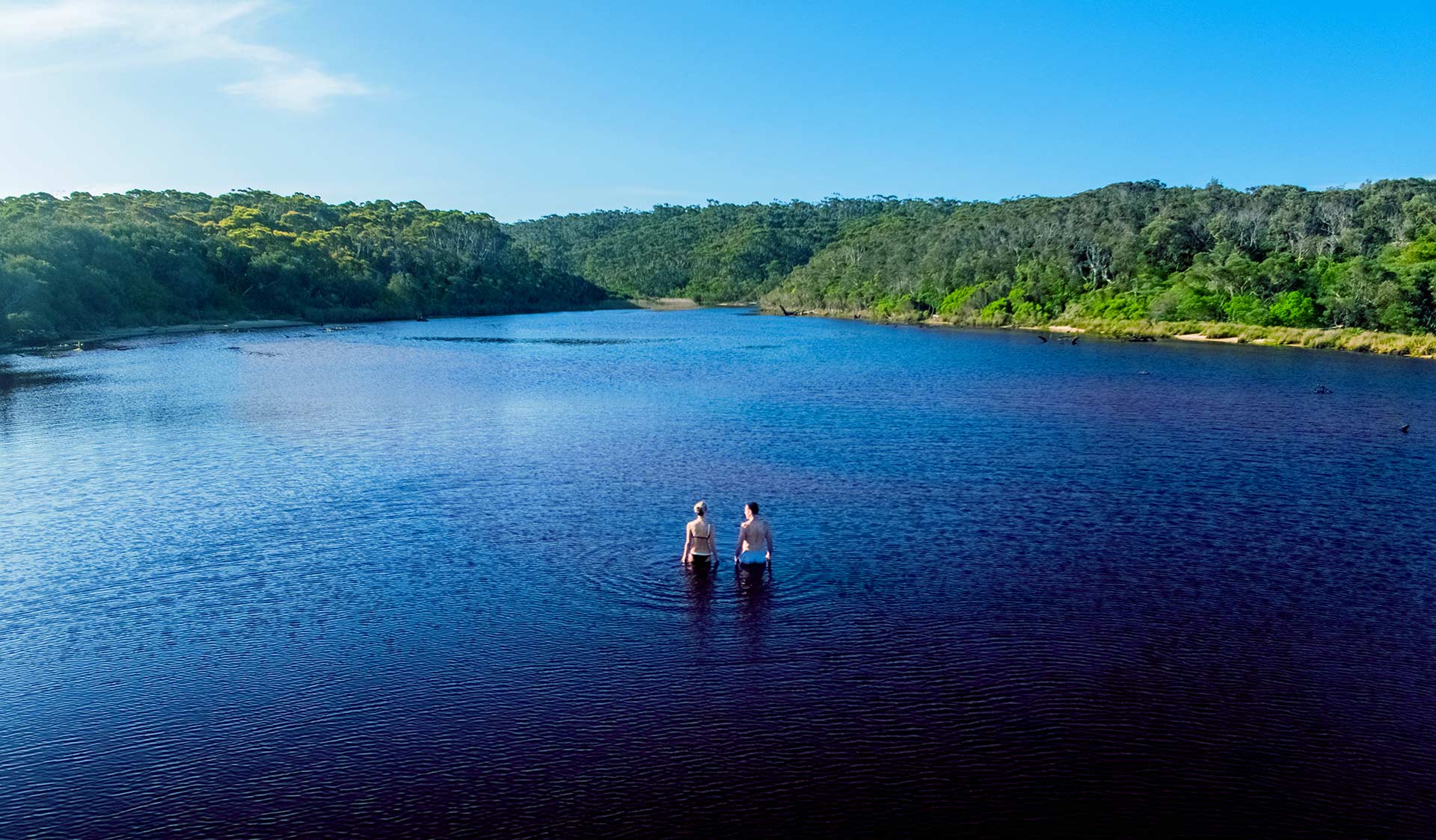 A couple walk out into a coastal lake at Croajingalong National Park. 