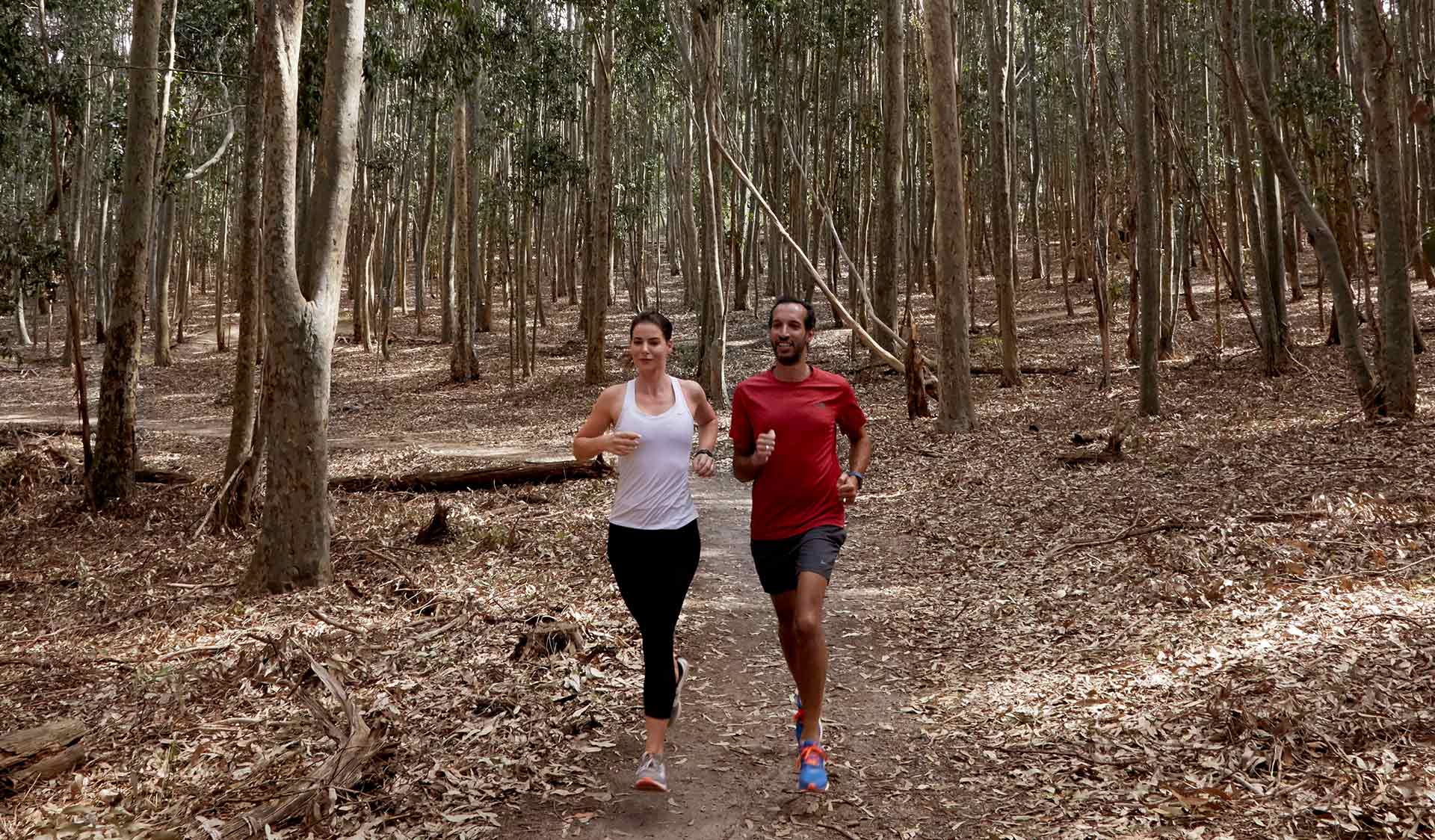 A couple run through the bush and leaves at Lysterfield Park.