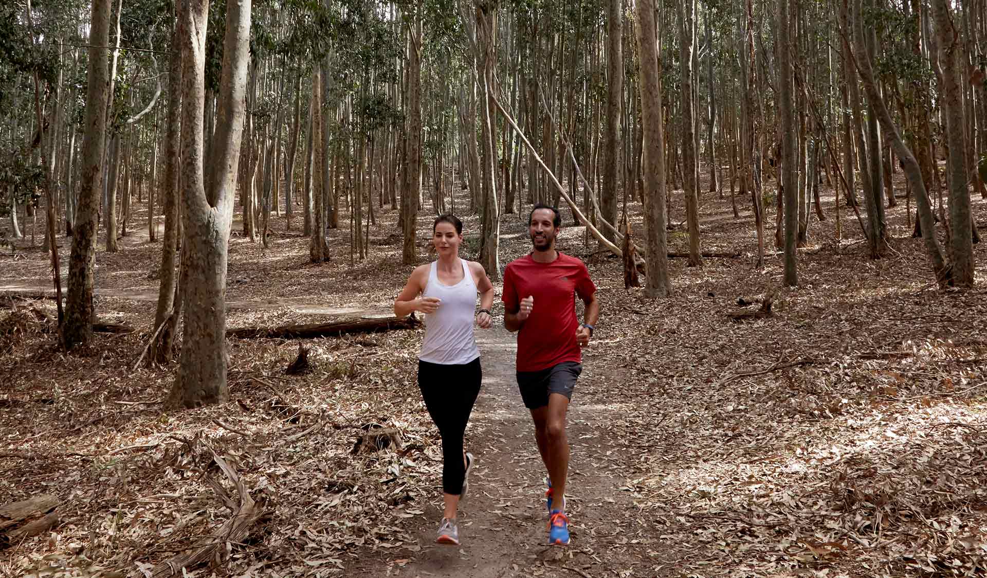 A couple run through the bush and leaves at Lysterfield Park. 