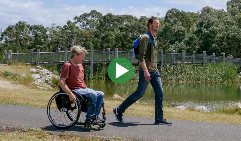 One man in a wheelchair and another walk along a path at Karkarook Park
