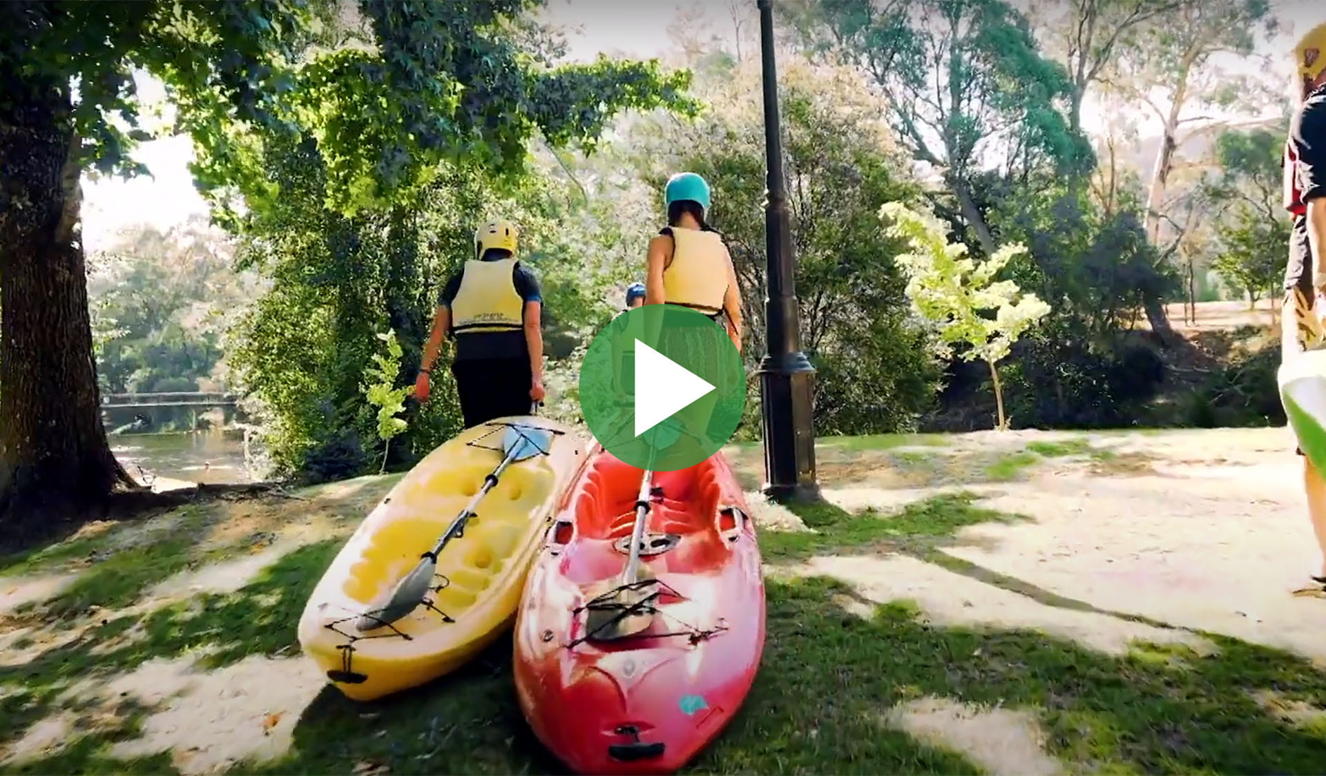 Still image from video of people pulling kayaks across grass with play icon overlay