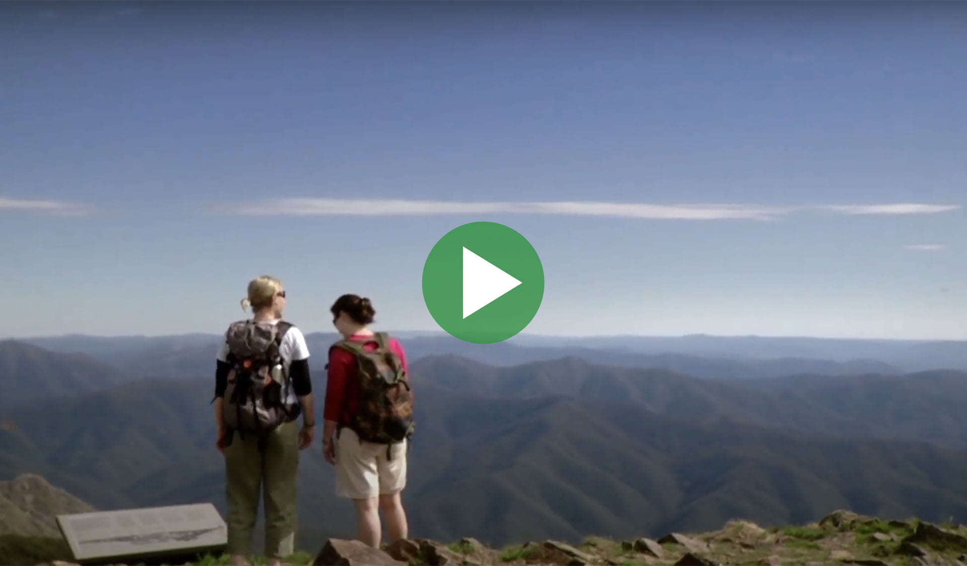 Still image from video of two people looking out at a mountain view with play icon overlay